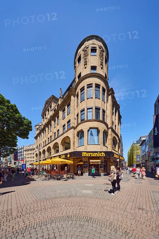 Historic commercial building Palatium, architect Wilhelm Kreis, sandstone building material, Merzenich bakery, corner building, shops, shopping, pedestrian zone, trees, pedestrians as accessories, blue sky, cloudless, intersection Hohe Straße with Gürzenichstraße, Cologne, district-free city, North Rhine-Westphalia, Germany