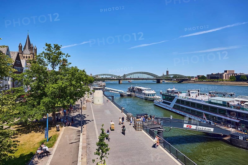 Rhine river, waterfront, sightseeing boats, general architecture, skyscrapers, modern architecture, church tower of Gross St. Martin, pedestrian and railway bridge Hohenzollern Bridge, trees, cyclists, pedestrians and visitors to a tour ship as a secondary motif, elevated perspective, blue sky, cirrus clouds, Deutz bridge, Leystapelwerft, Cologne, district-free city, North Rhine-Westphalia, Germany