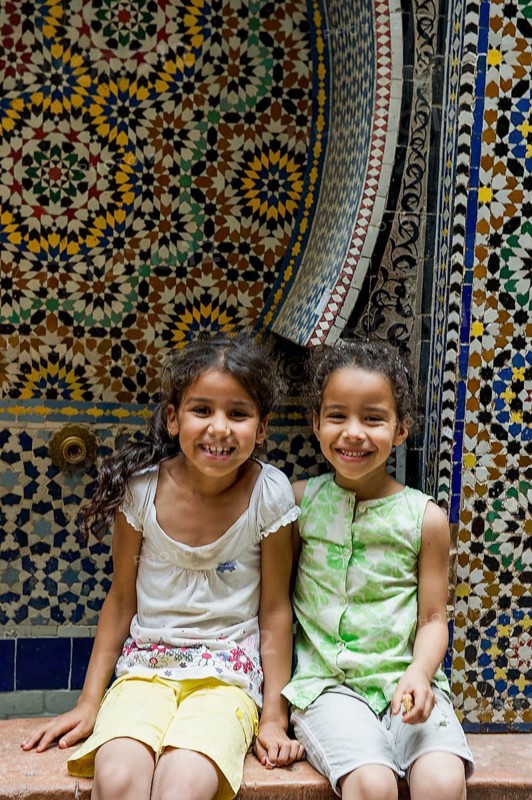 Two smiling girls in front of a wall with colorful tiles, alley in the old town, Souk, Fez El Bali, Medina, UNESCO World Heritage Site, Fez, Morocco