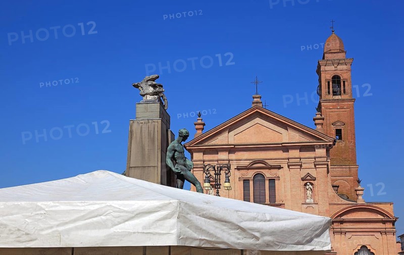 Monument with a statue in Piazza Unita and the Santo Stefano Collegiate Church in the city of Novellara, Emilia-Romagna, Italy