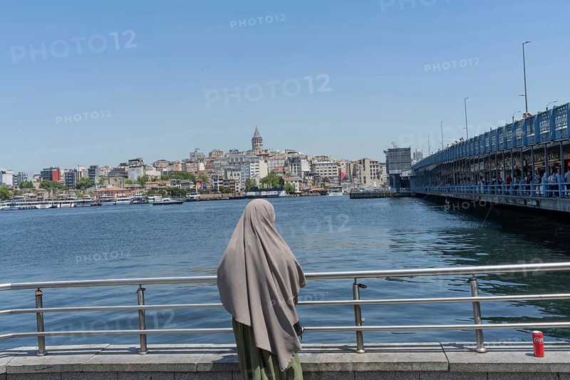 Istanbul, Turkey. June 23rd 2025. A Muslim women looks out across the Golden Horn towards the Galata Tower an iconic landmark of the largest city in Turkey