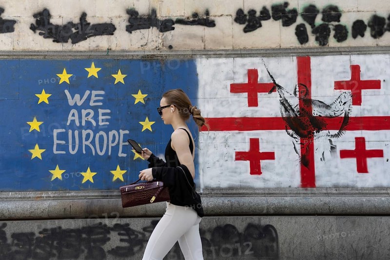 Tbilisi, Georgia. July 7th 2025. A woman walks past the flags of Georgia and the European Union along Shota Rustaveli Avenue near to Freedom Square, in central Tbilisi, Georgia