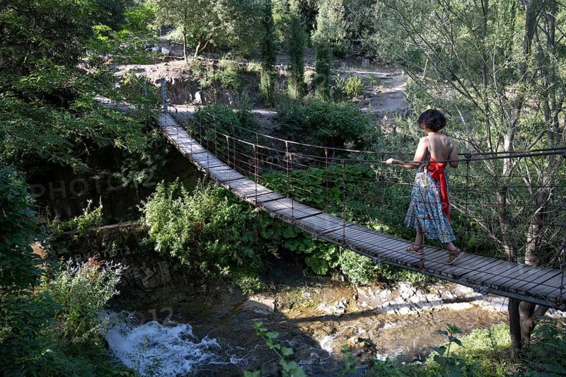 Tbilisi, Georgia. July 13th 2025. A foreign tourist crosses a wooden rope bridge inside the National Botanical Garden of Georgia in the Tsavkisis-Tskali Gorge, Tbilisi
