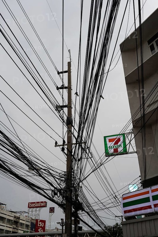 Bangkok, Thailand. March 4th 2025. A tangled mess of cables and wires used for phone and internet connections hanging from a pole in the street outside a 7 Eleven store in central Bangkok, Thailand