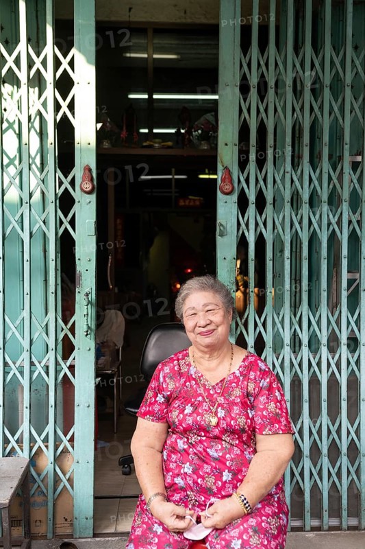 Bangkok, Thailand. March 18th 2025. A smiling older lady sitting outside a shop house in the streets of Talat Noi, Bangkok, Thailand, Asia