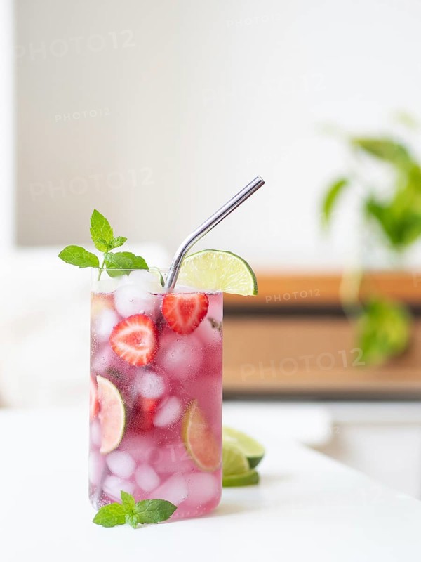 Strawberry mojito mocktail, full of ice, lime, mint, and drinking with a metal straw