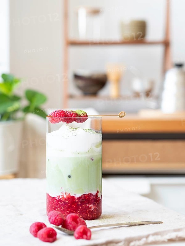 Raspberry matcha latte with ice, foam, fresh raspberries, and matcha powder on a counter