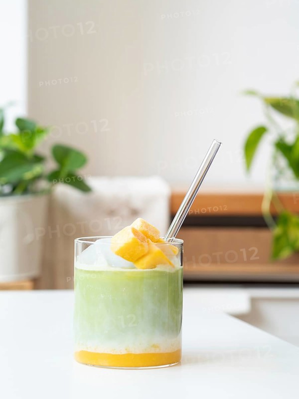 Iced matcha latte with tropical mango, milk, and clear straw in a glass