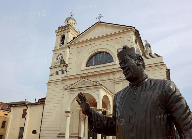 Italy, in the village of Brescello, statue of Don Camillo, portrayed by actor Fernand Joseph Desire Contandin, known as Fernandel, in front of the church of Santa Maria Nacente e San Genesio, Emilia Romagna, Italy