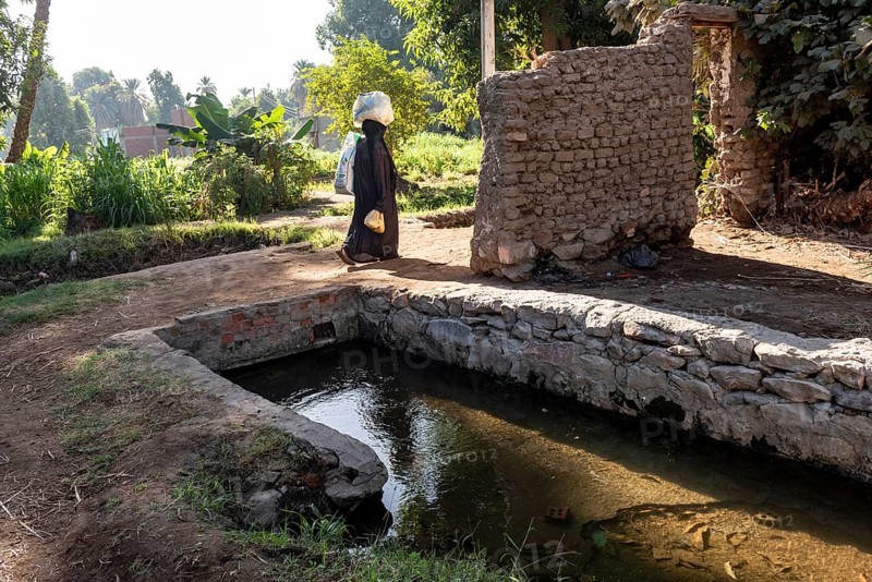 Aswan, Egypt. 9th December 2020 A Nubian woman carrying shopping walks past an irrigation channel on the Nile island of Elephantine, Aswan, Egypt