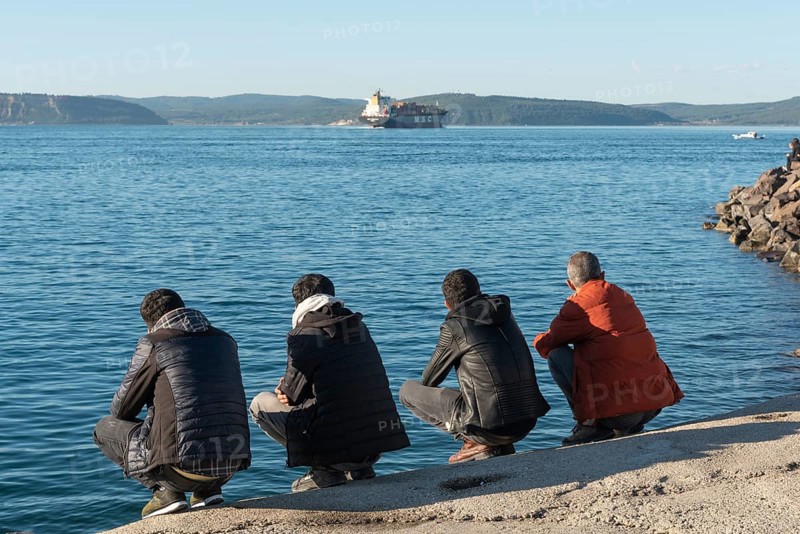 Canakkale, Turkey. February 18th 2022 Turkish men squatting beside the Dardanelles Straight opposite the Gallipoli Peninsular, the harbour of the port city of Canakkale, Western Turkey