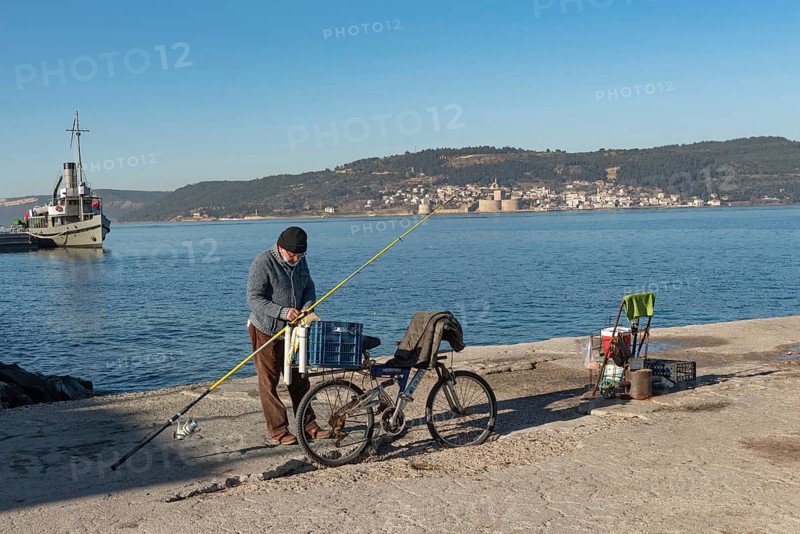 Canakkale, Turkey. February 18th 2022 A Turkish fisherman on the pier at Canakkale, with the Dardanelles Straight, Gallipoli Peninsula and Kilitbaher in the background
