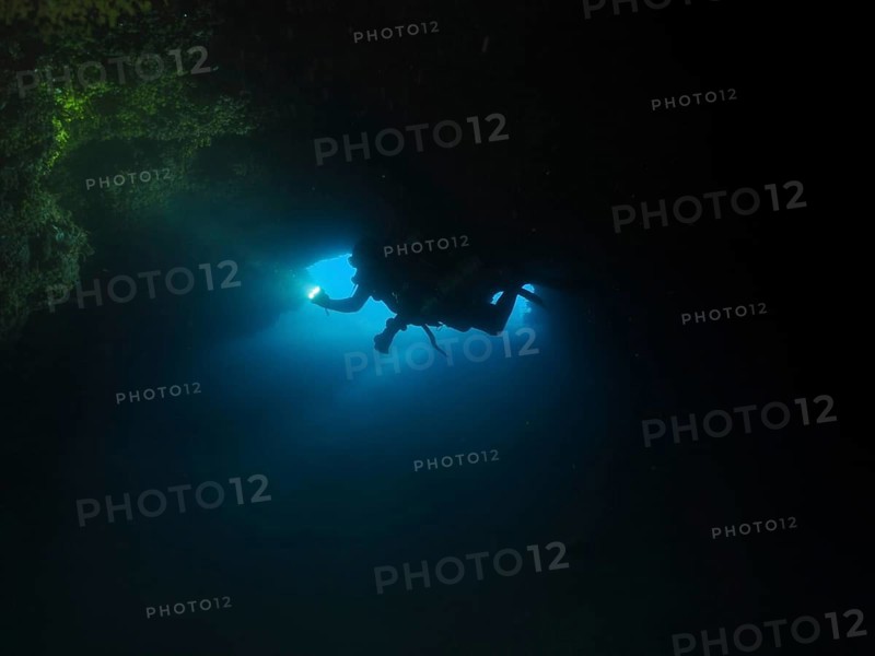 Diver, cave diver with lamp in dark underwater cave explores the surrounding area. Fraskeric dive site, Stoja, Pula, Croatia, Mediterranean