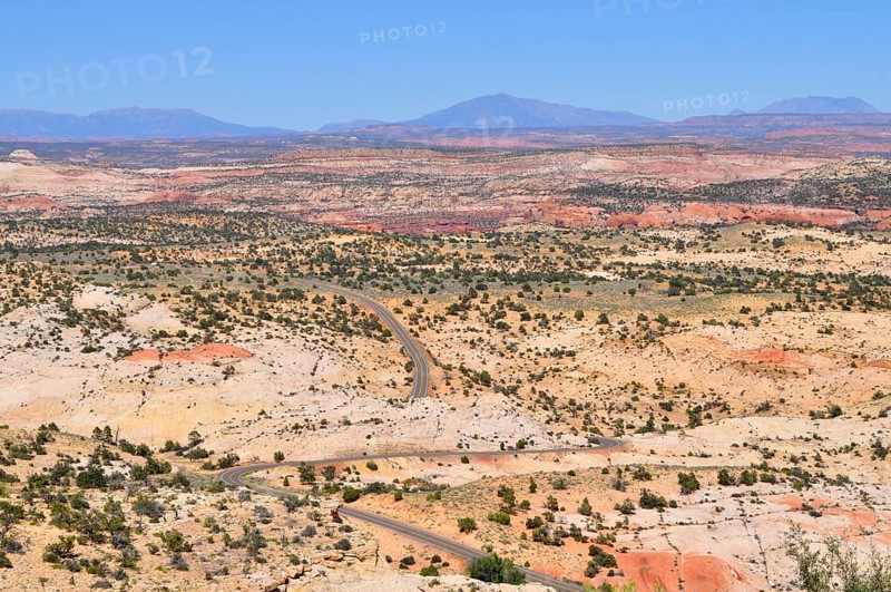 Curving road through dry, hilly landscape with reddish rocks under blue sky, Grand Staircase Escalante National Monument, Utah, USA