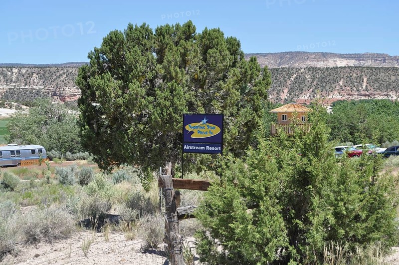 A tree with a sign in a rural landscape surrounded by green bushes and houses in the background, Shooting Star Drive In Airstream Resort, Bryce Canyon National Park, Utah, USA