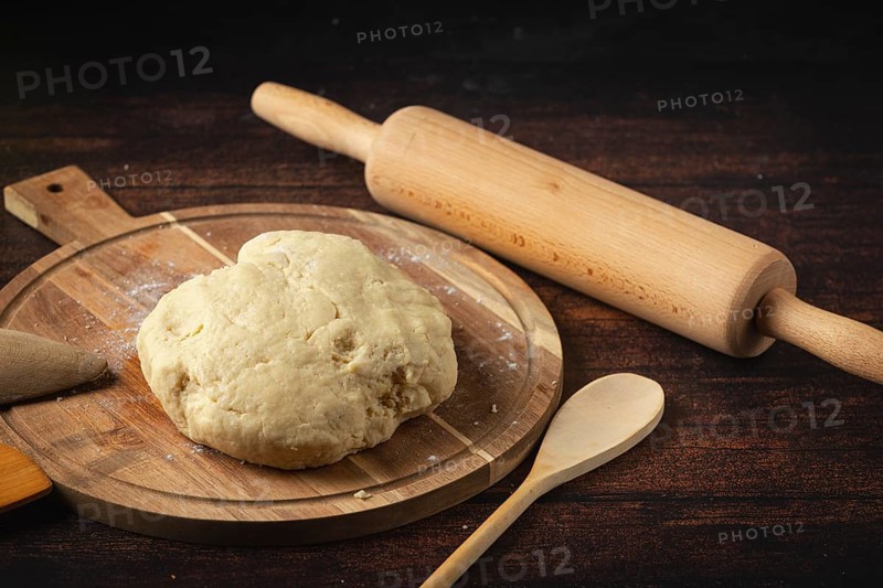 Fresh dough on a wooden table, ready to roll out, with a rolling pin