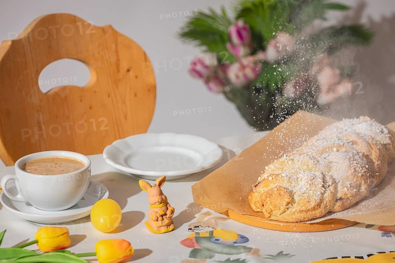 Yeast braid is sprinkled with sugar, breakfast table with coffee and decoration for Easter