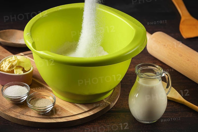 Sugar falls into a green bowl surrounded by baking ingredients