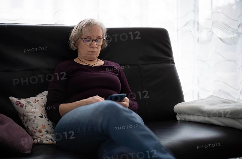 Elderly woman with glasses, gray hair, sitting on sofa and using smartphone, cell phone, Stuttgart, Baden-Württemberg, Germany