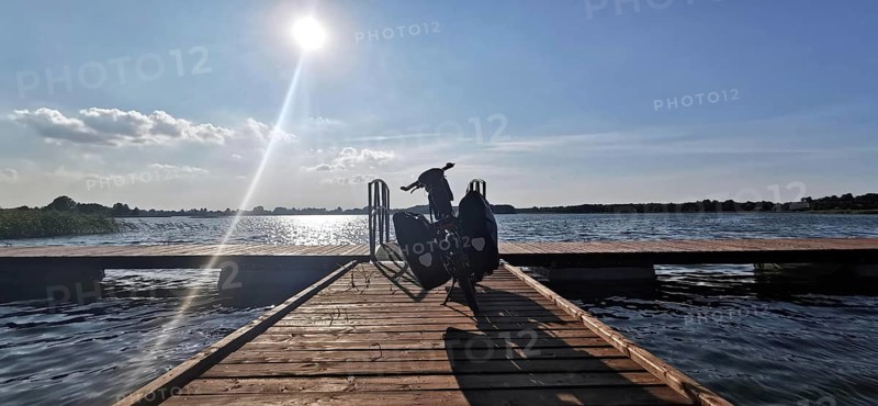 A bicycle is parked on a jetty leading out to the sunny lake, Masuria, Poland