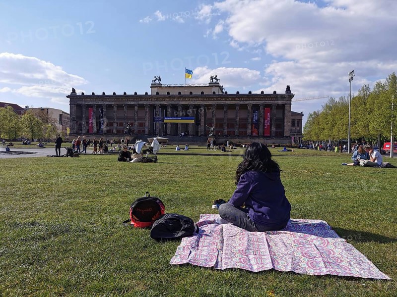 A woman sits on the meadow in front of the old museum on Museum Island in Berlin with the Ukrainian flag blowing in the wind, Berlin