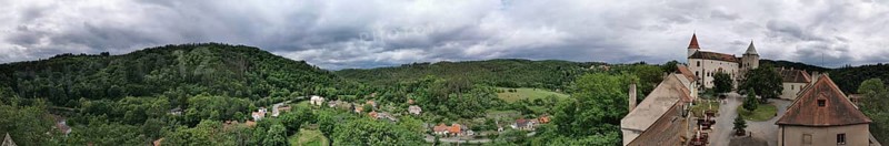 Panoramic view of a hilly landscape with a castle complex and thick greenery under cloudy sky, Krivoklat, Czech Republic