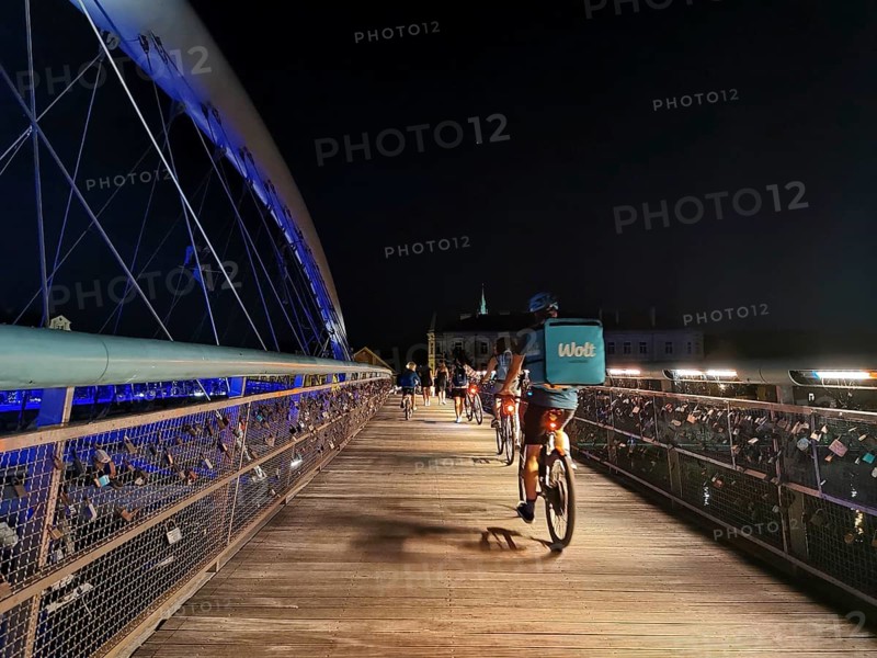 Delivery service Cyclists cross an illuminated bridge with railings on which countless padlocks hang with an urban background, Krakow, Poland