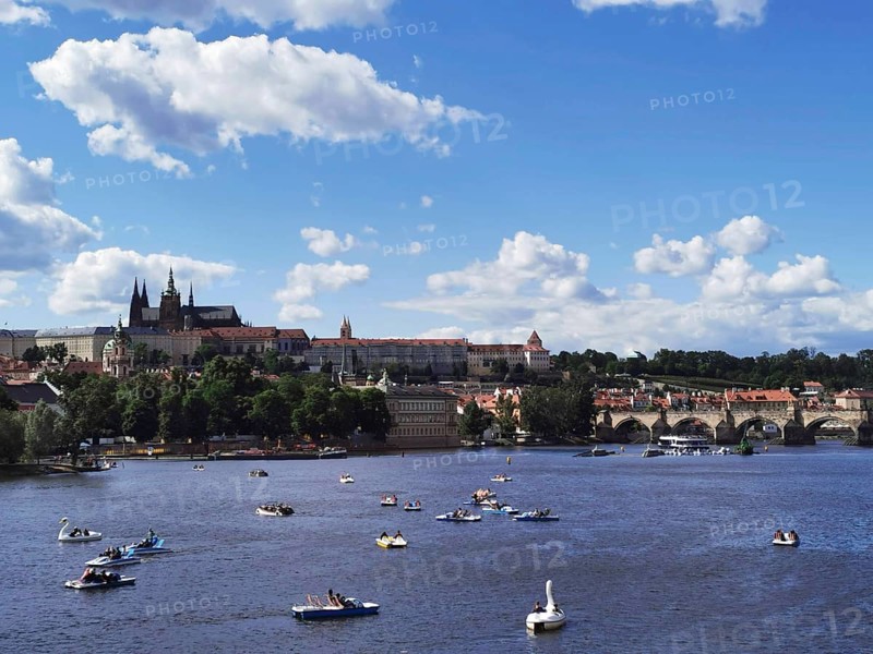 Summer hustle and bustle on the Vltava in Prague with Charles Bridge and Hradcany in the background, picturesque river landscape with boats, castle towers and an old bridge under a blue sky, Prague, Czech Republic