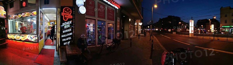 Panorama Lively evening street scene with illuminated snack bar and urban atmosphere, Pankow, Berlin