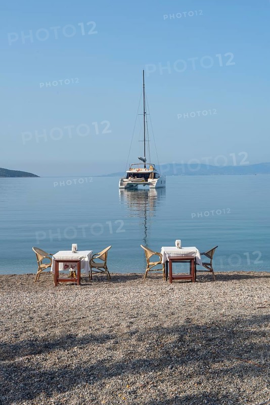 Bodrum, Mugla, Turkey. April 22nd 2022 Restaurant tables on the beach with a Catamaran moored in Bodrum harbour, a popular sailing and cruise destination along the Aegean coast in south west Turkey