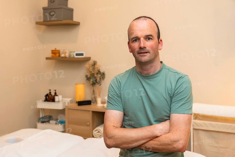 Male massage therapist owner standing with crossed arms in his wellness clinic, offering health, relaxation, and self care services in a professional spa environment