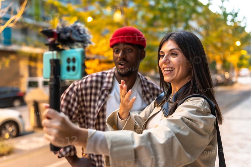 Happy young multiracial couple creating social media content, live streaming, and recording video outdoors on a city street with a smartphone on a gimbal