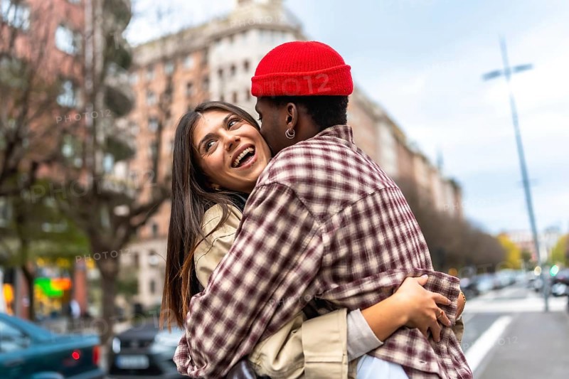 Young diverse couple embracing and laughing together on an urban street, sharing a moment of genuine happiness and showing affection while dating in the city