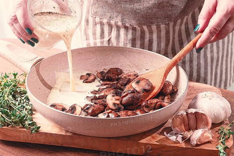 Cooking sauce with mushrooms, a woman pours cream into a pan with mushrooms, natural light, lifestyle