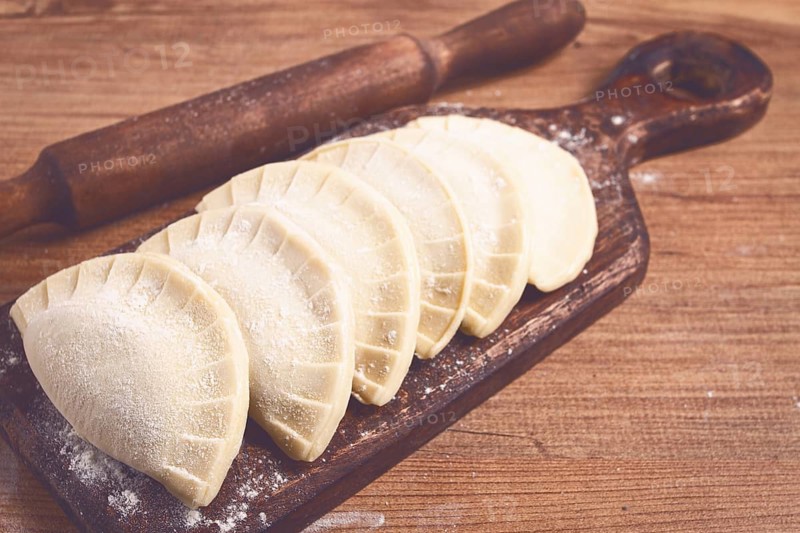 Raw chebureks, mini, on a cutting board, wooden table, close-up, no people