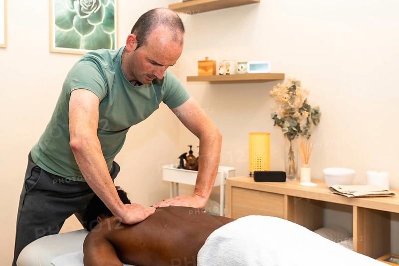 Male massage therapist providing therapeutic back treatment to a client lying face down in a calm wellness studio, focusing on relaxation, pain relief and holistic healing