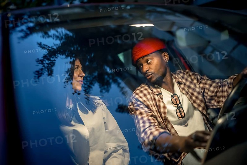 Interracial couple sharing a thoughtful conversation in a car at night, capturing authentic connection during an evening urban date that reflects modern, diverse relationships