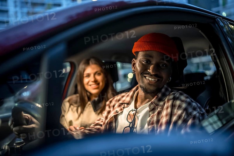 Young couple sharing a city rideshare at night, smiling in the car under street lights, enjoying an evening trip together, casual, happy and connected while traveling
