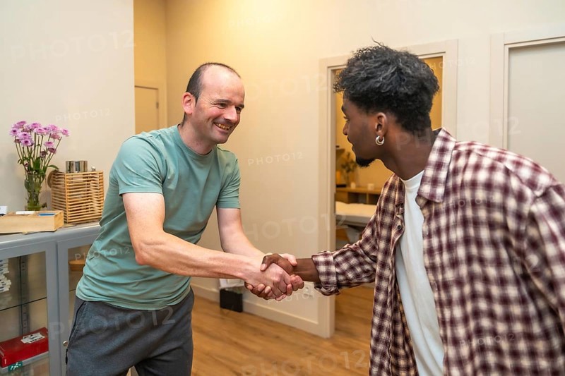 Two men from different backgrounds smiling and shaking hands in an office, symbolizing friendly partnership, trust, collaboration and successful multicultural business connection