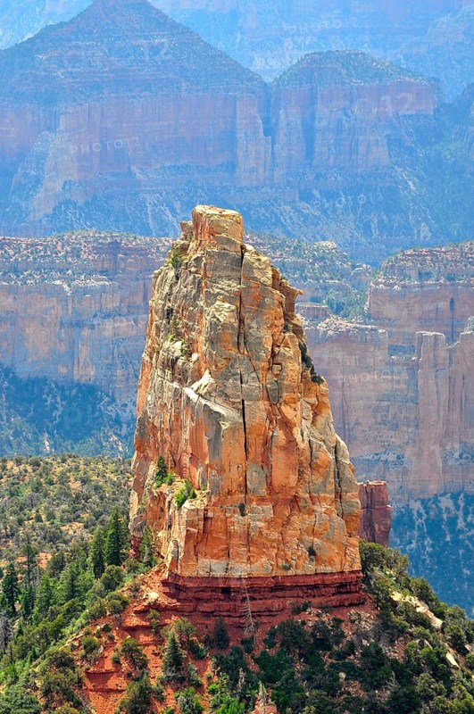 A massive rock rises steeply in a canyon landscape, surrounded by other rocks and sparse vegetation, Grand Canyon National Park, Arizona, USA
