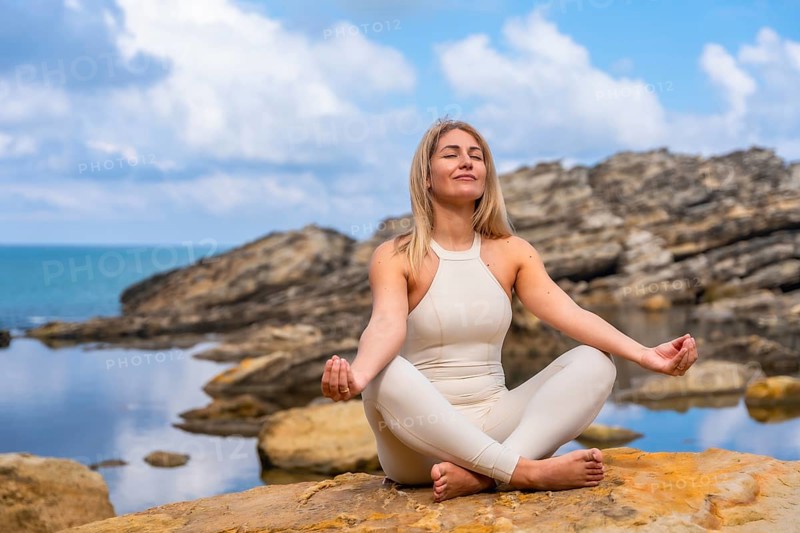 Woman in yoga pose on rocky coastline by the sea, practicing mindfulness and breathing for calm, balance and wellness amid serene ocean horizon and natural light