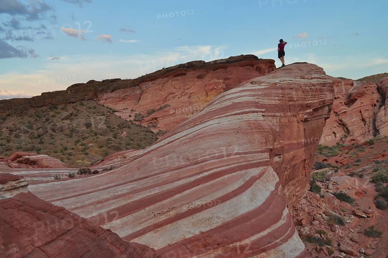 Person standing boldly on a striped cliff in the middle of the desert, Valley of Fire State Park, Nevada, USA