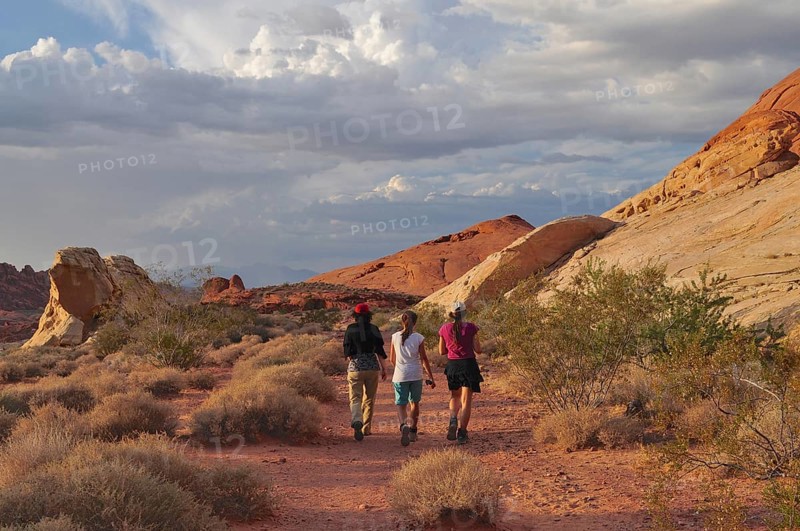 Three hikers on a trail through a desert landscape with clouds, Valley of Fire State Park, Nevada, USA
