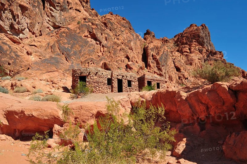 Abandoned stone houses nestled in a red rocky landscape under clear skies, Valley of Fire State Park, Nevada, USA