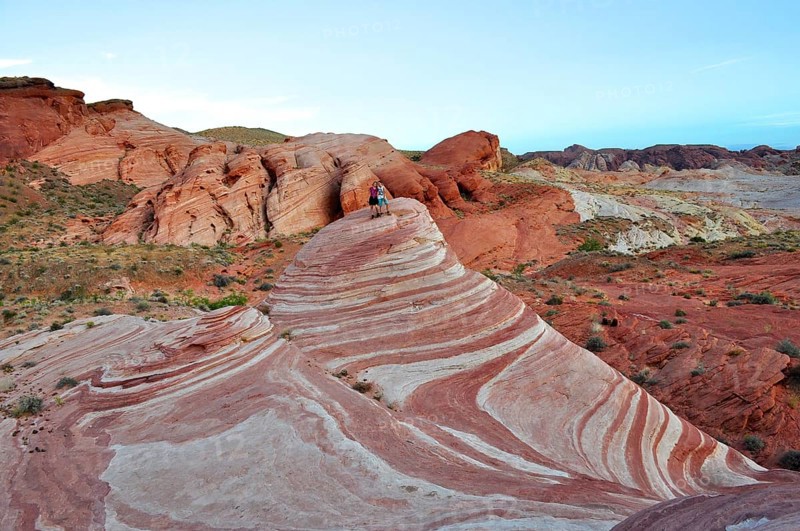 Two people standing on a striped rock formation in a desert landscape, Valley of Fire State Park, Nevada, USA