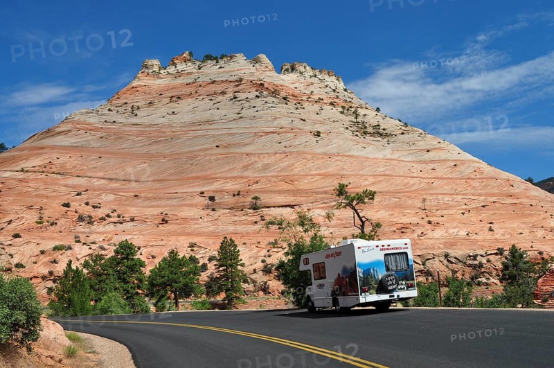 Motorhome drives along a road framed by red rocks and clear skies, Zion National Park, Utah, USA
