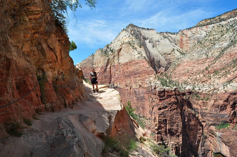 Person on a narrow hiking trail to Angel's Landing viewpoint along a red rocky mountain range, Zion National Park, Utah, USA