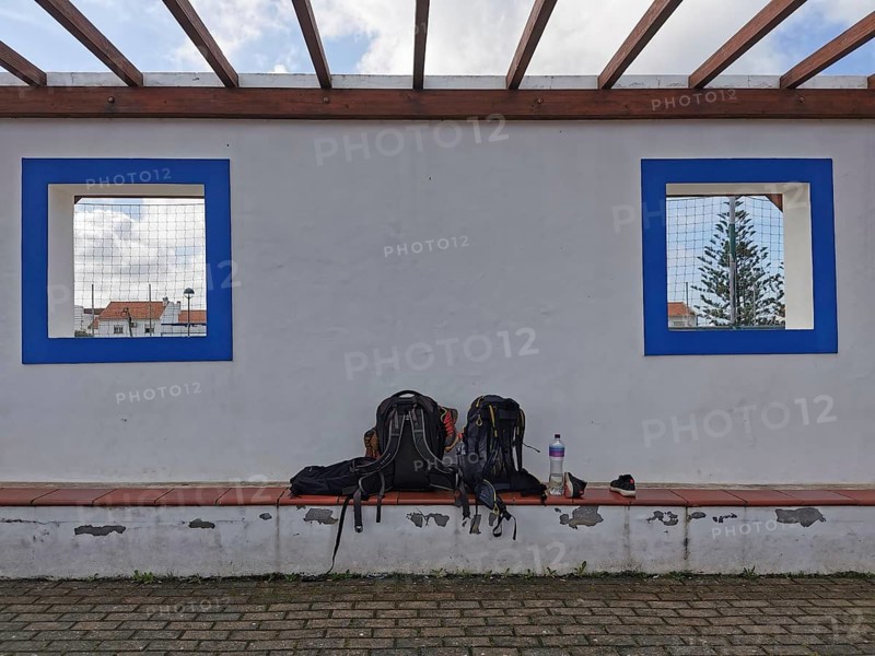 Two backpacks on a bench in front of a white wall with blue window cutouts, hiking on the Fisherman's Trail, Algarve, Portugal