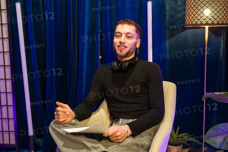 Young man wearing headphones around his neck and holding papers. Actively engaging. Communicating. And presenting while recording a video for social media or a podcast in a professional studio setting