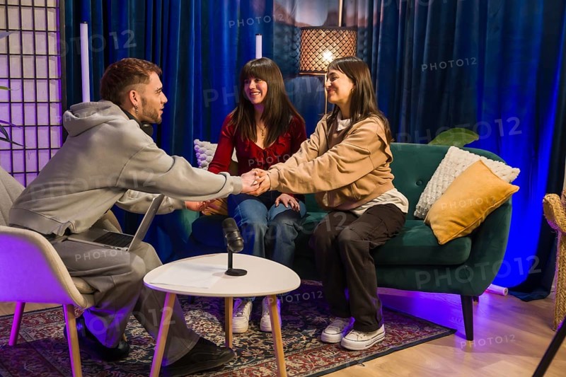 Three young content creators, a man and two women, sitting in a modern studio, recording a podcast or social media broadcast, talking and engaged in conversation